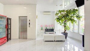 A clean, modern lobby with a vending machine, elevator, white cushioned seating, and a large potted plant. - Stylish DBL Suite Escape W/ Free Wifi and Parking (Jakarta)