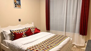 Ein Bett mit einem gemusterten Überwurf, einem weißen Kopfteil und roten Kissen.