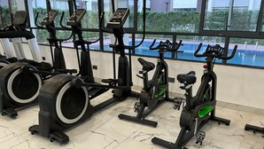 Ein Fitnessstudio mit Ergometer und Crosstrainern, großen Fenstern und Blick auf einen Pool.