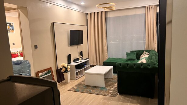 Ein modernes Wohnzimmer mit einem Flachbildfernseher, einem grünen Sofa, einem weißen Couchtisch und einem großen Fenster mit Vorhängen.