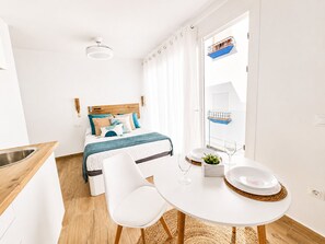 Ein modernes Hotelzimmer mit Bett, Esstisch mit Stühlen, einer kleinen Küchenzeile und einem Balkon mit Fenster.