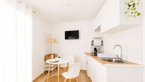 A compact kitchen with a dining area, white cabinetry, a flat-screen TV, and a wooden floor. - CREA Conil Apartments III (Conil de la Frontera)