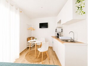 Eine kompakte Küche mit Essbereich, weißen Schränken, einem Flachbildfernseher und Holzboden.