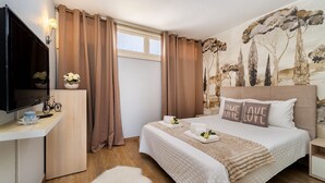 Ein Schlafzimmer mit einem Bett, einem Fernseher, einem Schreibtisch und einem Fenster mit Vorhängen.