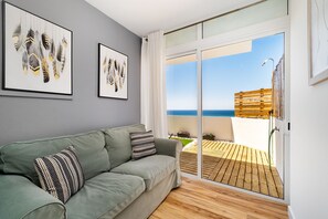 A modern living room with a green sofa, two framed artworks, a sliding glass door leading to a wooden deck. - Penthouse 100 meters from the beach (Albufeira)
