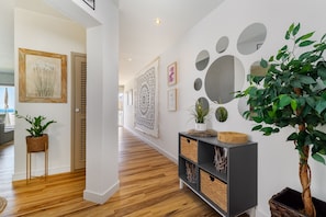 A hallway with wooden flooring, a grey console table with baskets, a potted plant, and wall art including a large abstract design and a framed picture. - Penthouse 100 meters from the beach (Albufeira)