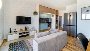 Ein modernes Wohnzimmer mit einer Couch, einem Fernseher und einer Küche im Hintergrund.