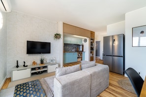 Ein modernes Wohnzimmer mit einer Couch, einem Fernseher und einer Küche im Hintergrund.