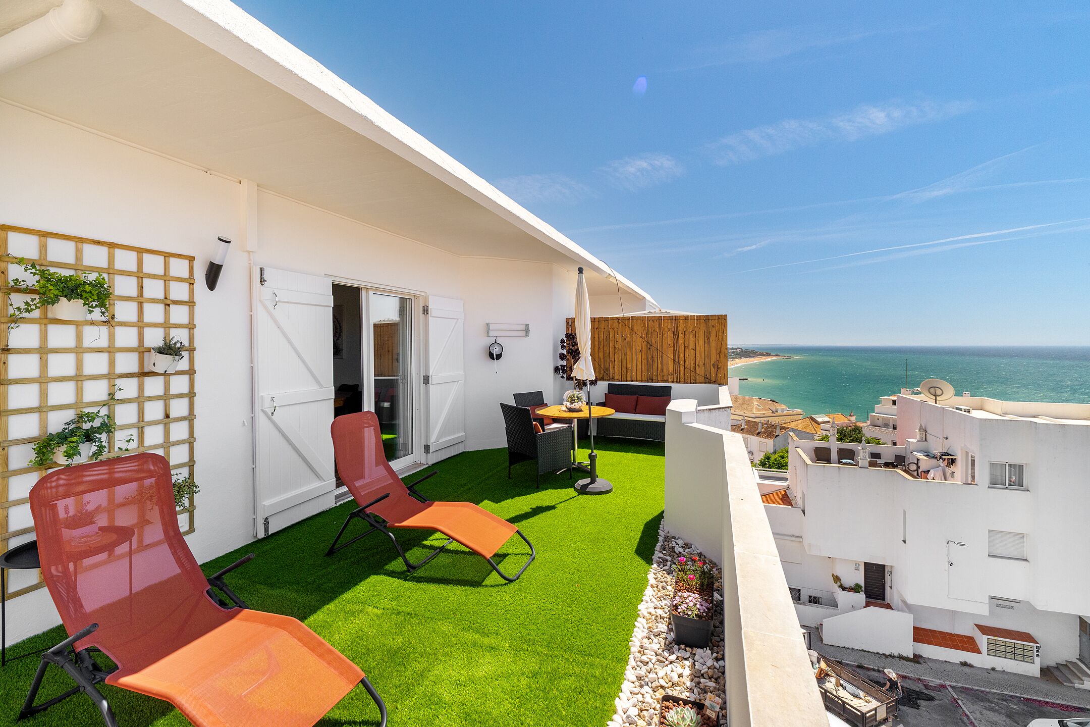 A balcony with artificial grass, two red chairs, a table, and a sofa.