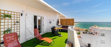 A balcony with artificial grass, two red chairs, a table, and a sofa.