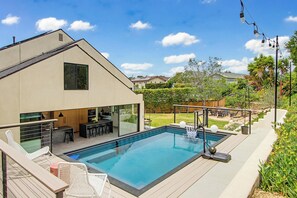 Ein modernes Haus mit Swimmingpool, Sitzgelegenheiten im Freien und einem gepflegten Garten.