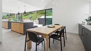 A modern kitchen with a dining area, large windows, and a view of greenery. - Modern Encinitas Retreat (Encinitas)