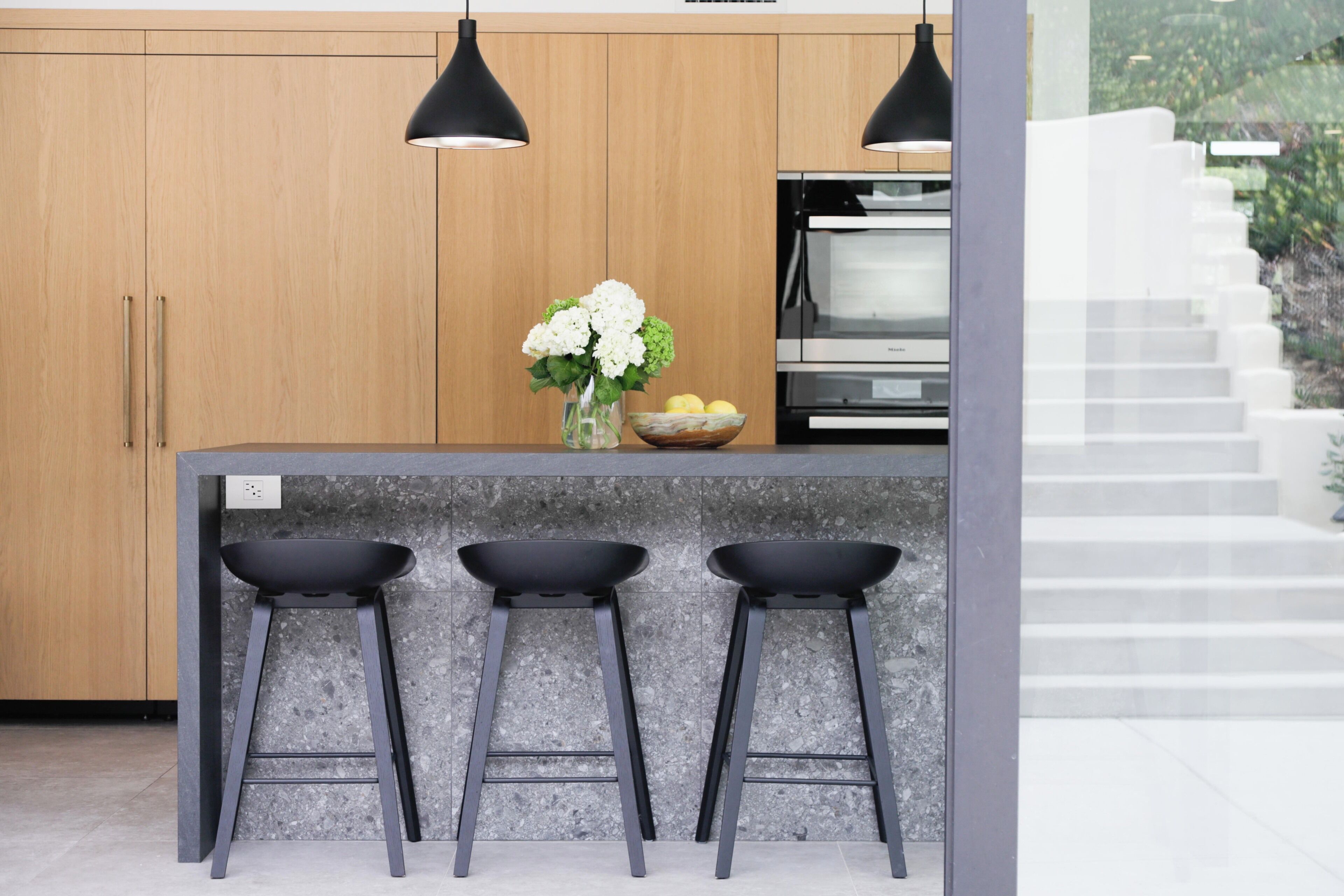 A modern kitchen with wooden cabinets, a granite countertop, and three black bar stools.