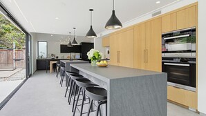 A modern kitchen with a central island, bar stools, pendant lighting, and a large oven. - Modern Encinitas Retreat (Encinitas)