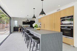 Eine moderne Küche mit Kochinsel, Barhocker, Pendelleuchten und einem großen Backofen.
