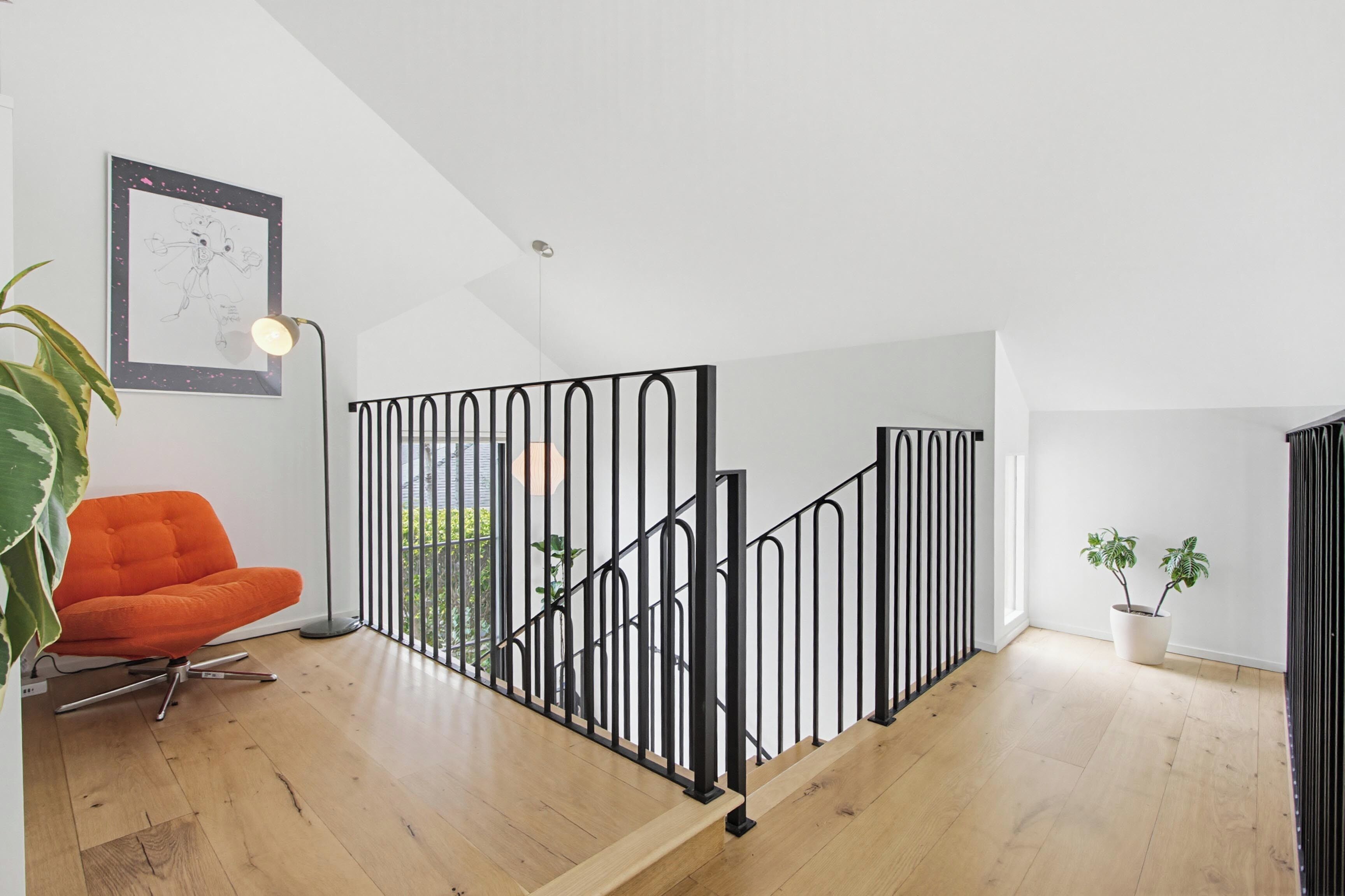 Un intérieur moderne avec un escalier, une œuvre d’art encadrée, un fauteuil orange vif et une plante en pot.