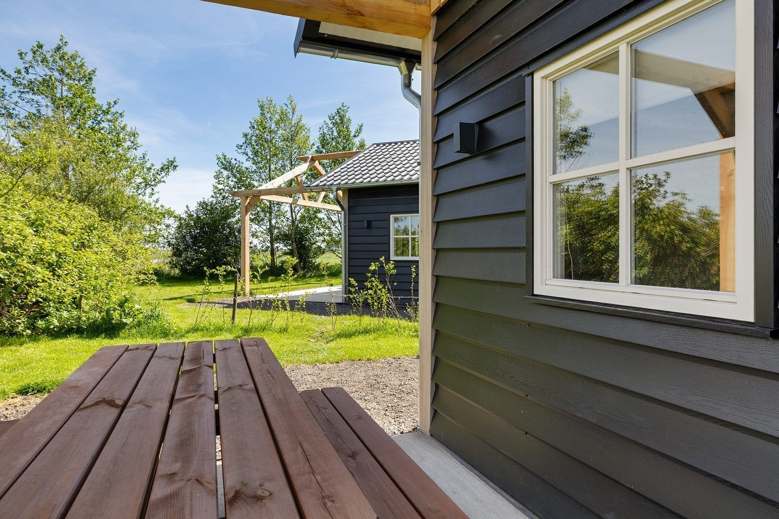 Eine Holzterrasse mit Tisch, ein Haus mit dunkler Holzverkleidung und ein Fenster.