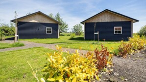 Two cabins with a gravel path leading to them, surrounded by grass and plants.