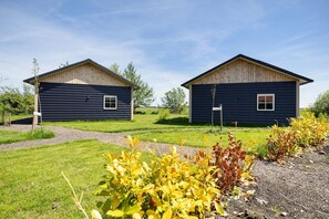 Two cabins with a gravel path leading to them, surrounded by grass and plants.