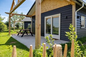Ein Haus mit einer Holzpergola, einer Terrasse mit Picknicktisch und einer Schiebetür.