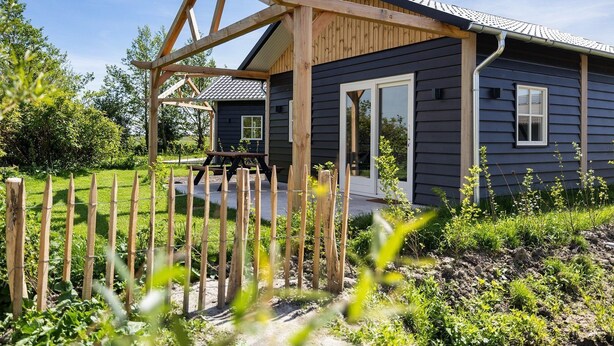 A house with a wooden deck, a picnic table, and a fenced garden.