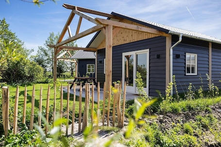 A house with a wooden deck, a picnic table, and a fenced garden.. De Wartenster - Vakantiehuisje