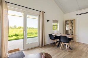 Ein Zimmer mit Esstisch, Stühlen, einem Bücherregal und Blick auf ein grünes Feld durch eine Schiebetür.