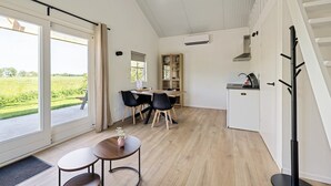 A modern kitchen with a dining area, a built-in bookshelf, and a view of a green field.