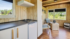A wooden cabin interior with a kitchen, a dining area, and a window with a view of greenery. - Camping de Wartenster - Pipowagen (Wartena)