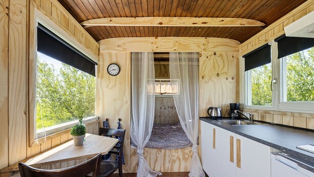 A compact room with a bed, a dining table, chairs, a sink, and a clock on the wall. - Camping de Wartenster - Pipowagen (Wartena)