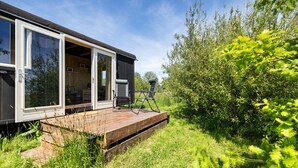 A modern mobile home with a deck, large windows, and a view of the surrounding greenery. - Camping de Wartenster - Pipowagen (Wartena)