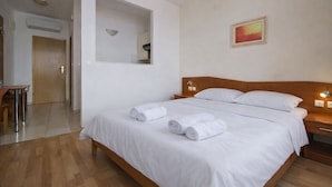 Une chambre d’hôtel avec un lit en bois, du linge de lit blanc, un miroir, un tableau et un bureau avec des chaises.