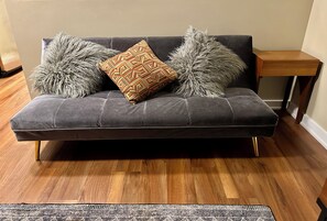 Ein graues Sofa mit flauschigen Kissen und einer gemusterten Decke, das auf einem Holzboden steht.