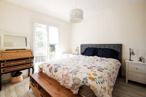 Ett sovrum med en säng, en byrå, en bänk, en lampa och en hängande taklampa.