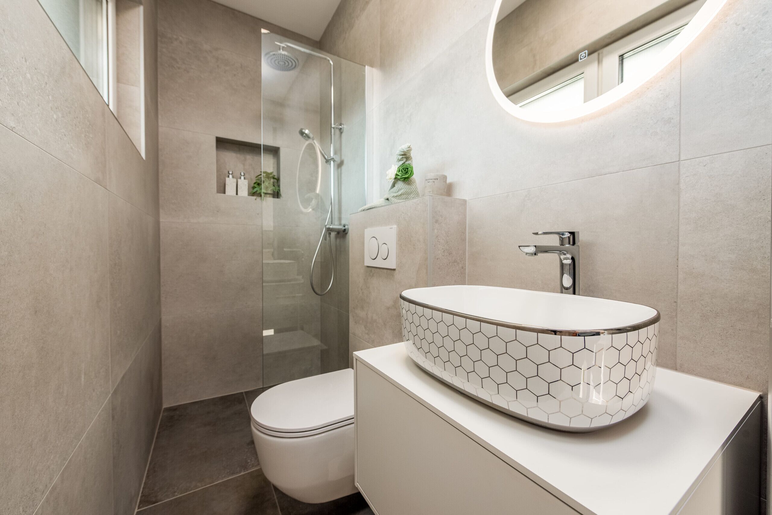A modern bathroom with a glass-enclosed shower, a white toilet, and a hexagonal-patterned sink.