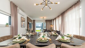 Ein Essbereich mit einem langen Tisch, gedeckt für eine Mahlzeit, einer Kandelaber und Blick ins Freie.