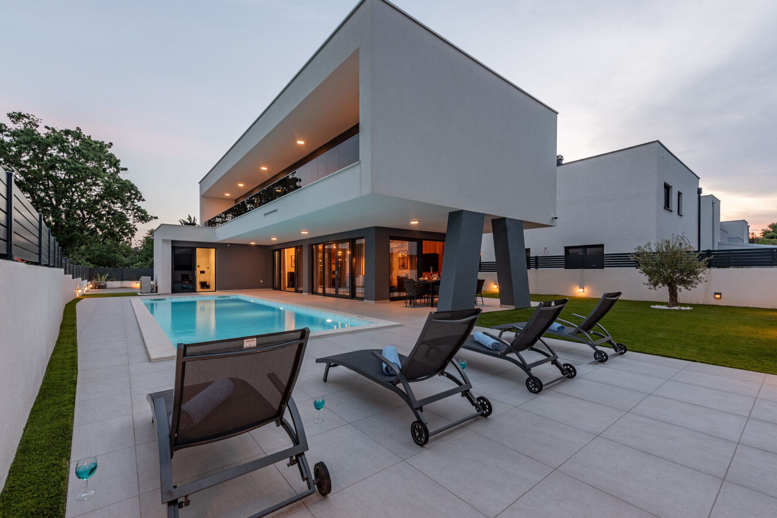 A modern two-story house with a swimming pool, outdoor seating, and a well-maintained lawn.