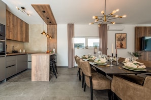 A modern kitchen with wooden cabinets, a central island, pendant lighting, and a dining area with a table set for six. - Villa Salt2 Zadarvillas (Nin)