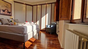 A bedroom with a large bed, a desk, and a chair. There is a painting on the wall and a radiator on the floor. - Cypress House (Pescia)