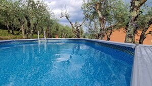 A clear swimming pool surrounded by trees and a building with a tiled exterior. - Cypress House (Pescia)