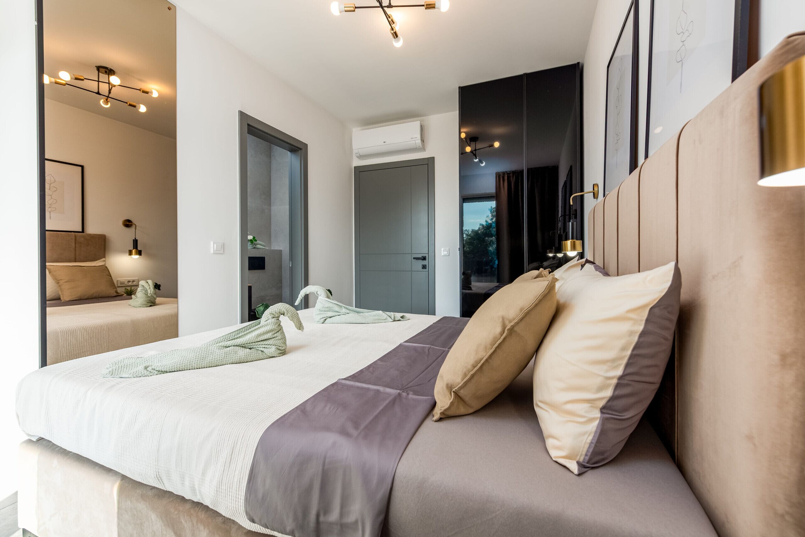 A modern bedroom with a large bed, bedside tables, a wardrobe, and an air conditioning unit.