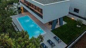 Una casa moderna de dos pisos con piscina, mobiliario de exterior y césped cuidado.