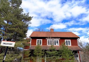 A red wooden building with a sign reading 'INGATORP' and a clear blue sky with clouds.