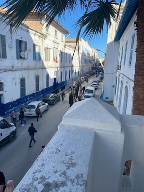 Vista de calle con edificios, coches aparcados y peatones.