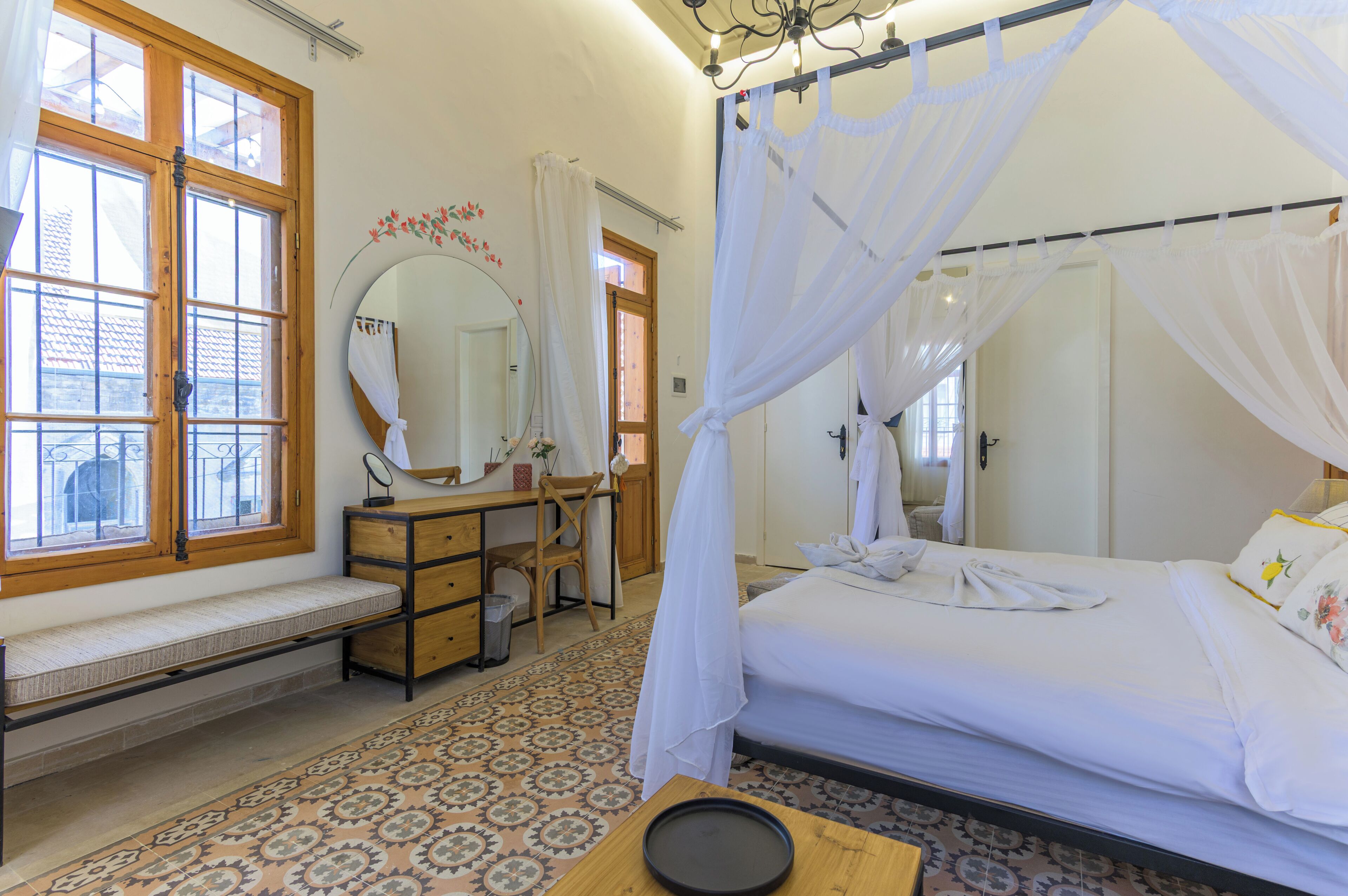 Quarto com cama, mesa de cabeceira, cadeira, escrivaninha, espelho e janela com cortinas.