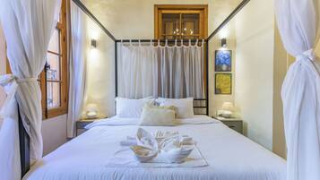 A neatly made bed with white linens and a towel arrangement, a wooden-framed window, and two bedside lamps.