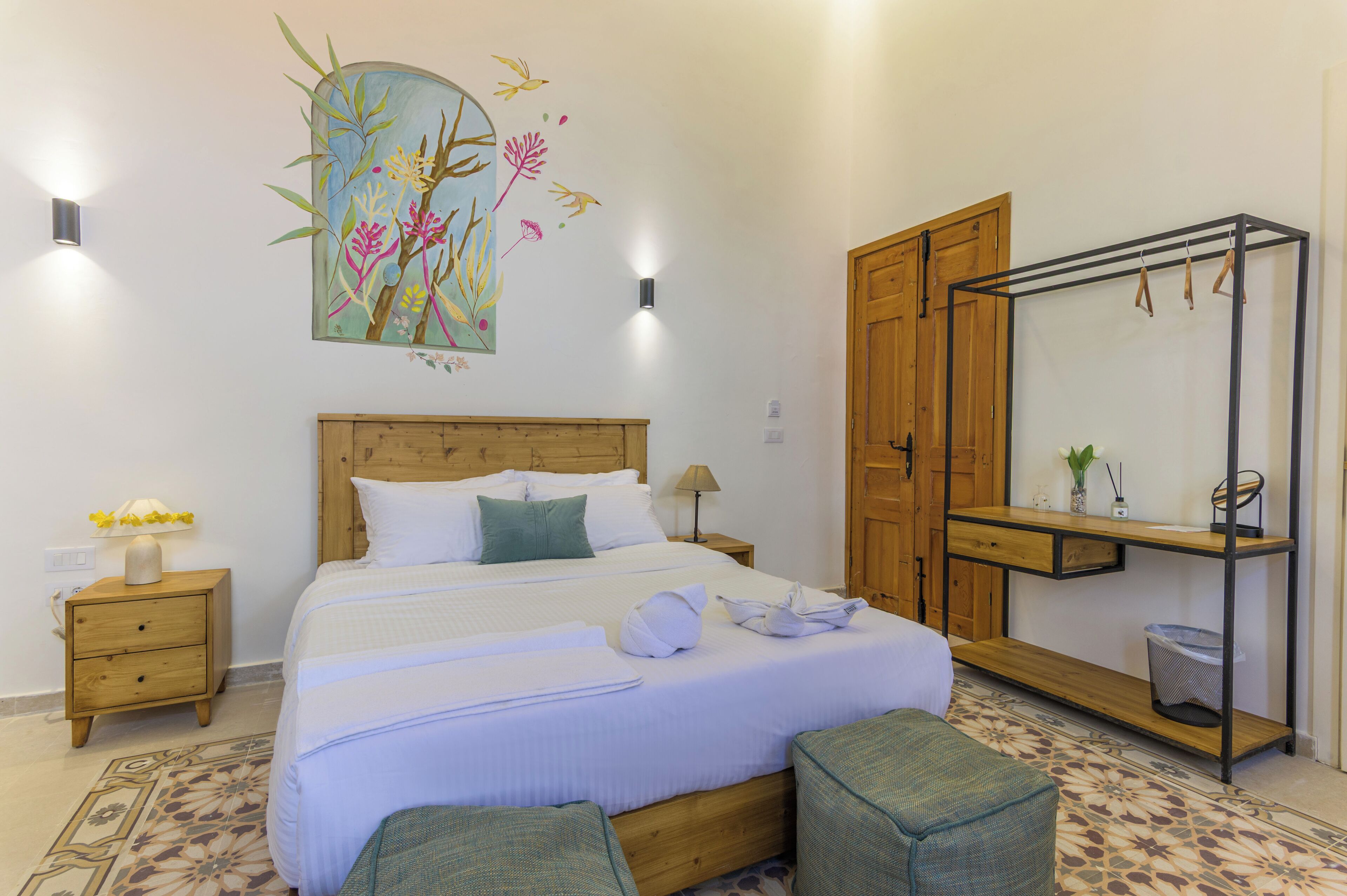 A neatly arranged bedroom with a bed, bedside tables, a wooden wardrobe, a mirror, and a wall decoration.