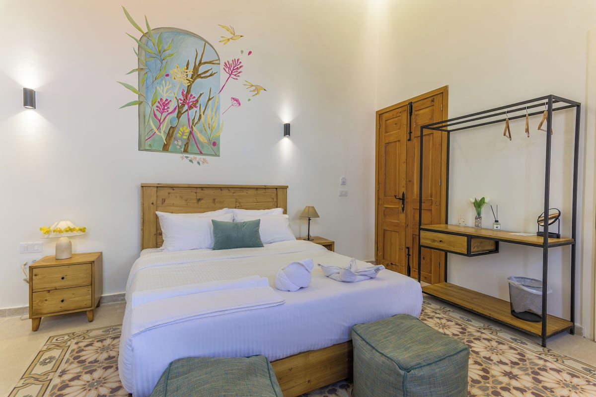 Un dormitorio ordenado con cama, mesitas de noche, un armario de madera, un espejo y un adorno en la pared.