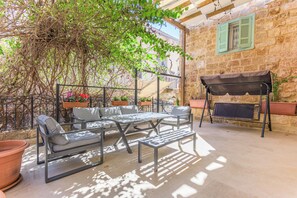 An outdoor patio with a table and chairs, a swing, and a stone wall. - Les Bougainvilliers Studios in Batroun (Batroun)