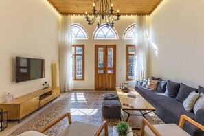 A spacious living room with a large sofa, a wooden coffee table, and a flat-screen TV mounted on the wall. - Les Bougainvilliers Studios in Batroun (Batroun)